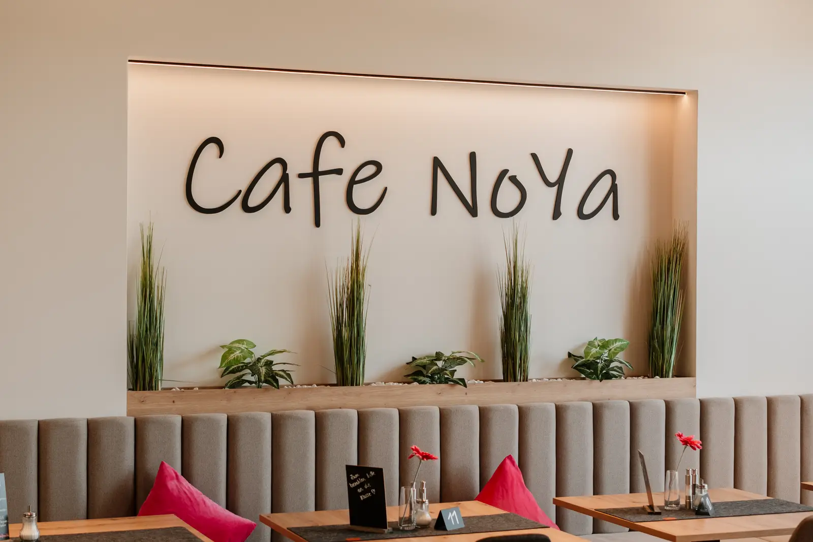 Gastraum des Café NoYa mit „Cafe NoYa“-Schriftzug an der Wand und gepolsterter Sitzbank