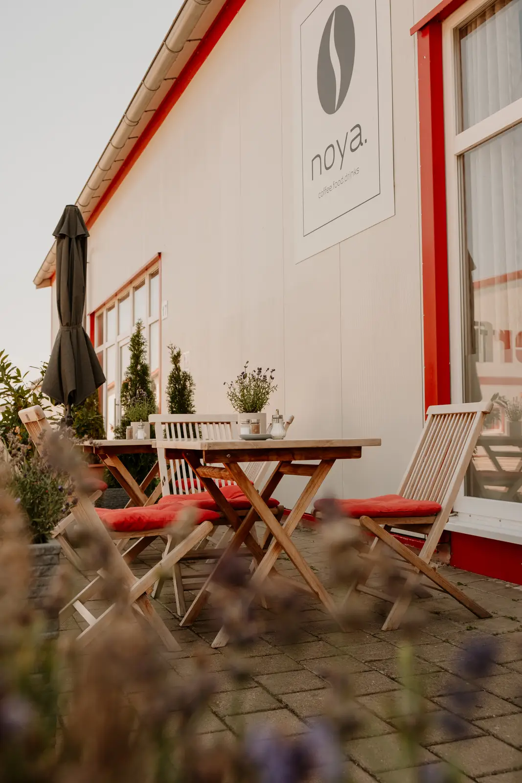 Außenbereich des Café NoYa mit Terrasse und Logo an der Fassade